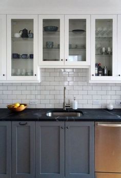 a kitchen with white cabinets and black counter tops in front of a bowl of fruit