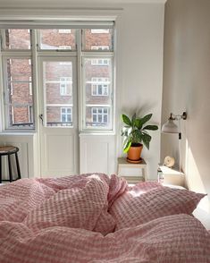 a bed in a room with a pink comforter on it and a potted plant next to the window