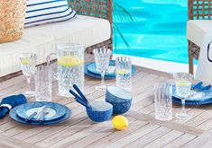 an outdoor table set with blue and white dishes, glasses, lemon wedges and silverware