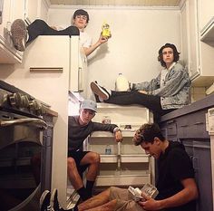 three young men sitting on top of bunk beds in a room with white walls and cabinets