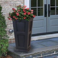 a tall planter with red flowers in front of a door