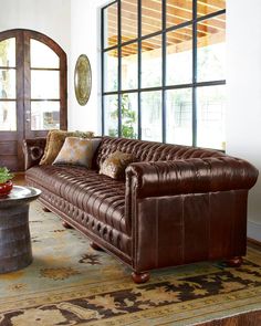 a brown leather couch sitting in front of a window with lots of pillows on it