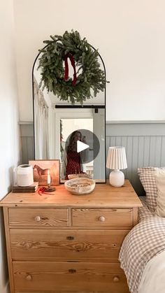 a bedroom with a dresser, mirror and christmas wreath on the top of it's headboard