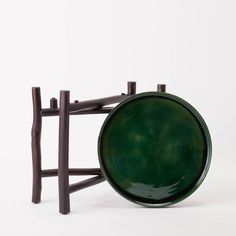 a green bowl sitting on top of a wooden stand next to a white wall and two brown poles