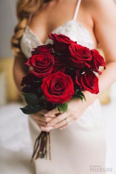 a woman in a wedding dress holding a bouquet of red roses with her hands on her hips