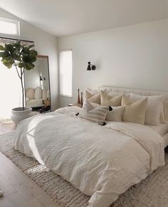 a large bed sitting in the middle of a bedroom next to a mirror and potted plant