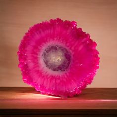 a pink flower sitting on top of a wooden table next to a light brown wall