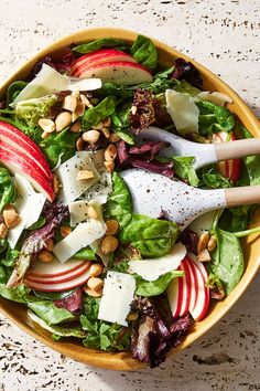 a salad with apples, cheese and nuts in a wooden bowl on a marble surface