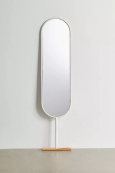 a mirror on a stand with a wooden stick in the foreground and a white wall behind it