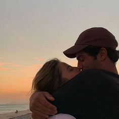 a man and woman embracing each other on the beach at sunset with people in the background