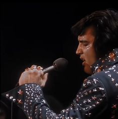 elvis presley singing into a microphone with stars all over his shirt and black jacket on