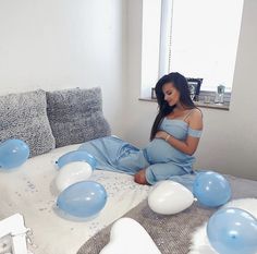 a pregnant woman sitting on a bed with balloons