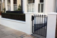 a white house with black iron fence and window boxes on the front door, next to a brick sidewalk