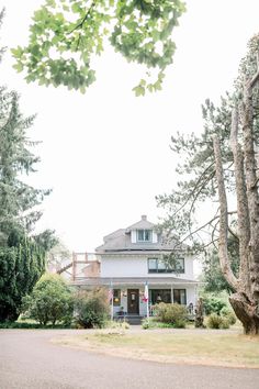 a large white house sitting on the side of a road next to some tall trees