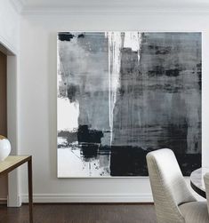 an abstract painting hangs on the wall above a dining room table with two white chairs