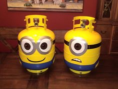 two yellow and blue plastic tanks with eyes on them sitting on a wooden floor in front of a red wall