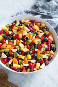 a white bowl filled with fruit salad on top of a counter next to a wooden spoon