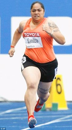 a woman running on a race track in an orange shirt and black shorts with tattoos