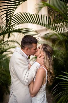 a bride and groom kissing in front of palm trees