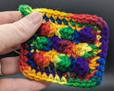 a hand is holding a crocheted multicolored pouch