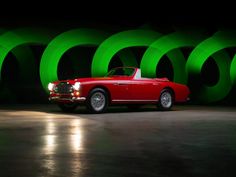 an old red car is parked in front of some green wallpaper and circular lights