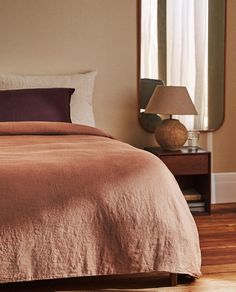 a bed sitting in a bedroom next to a mirror and lamp on top of a wooden floor