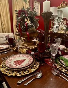 a dining room table set for christmas with plates, silverware and candlesticks