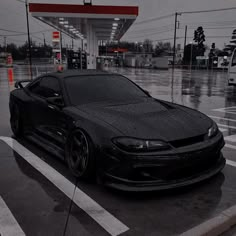 a black sports car parked in front of a gas station on a wet parking lot