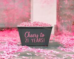 a bucket filled with pink shredded paper on top of a cement floor covered in confetti