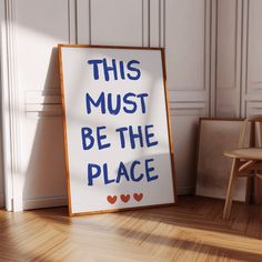 this must be the place sign next to a wooden chair in a room with white walls