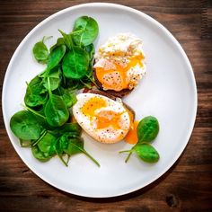 two eggs and spinach on top of a white plate next to some green leaves