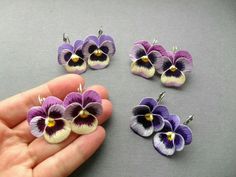 a hand is holding four small purple and white pansyflowers, one being held in front of the other