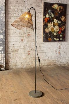 a floor lamp with a metal shade on it in front of a white brick wall