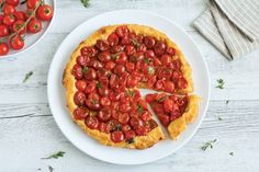 a tomato tart on a white plate next to some cherry tomatoes