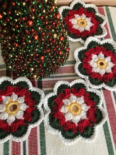 four crocheted flowers sitting on top of a plaid tablecloth next to a christmas tree