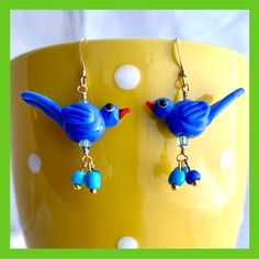 two blue birds are hanging from earrings on a yellow cup