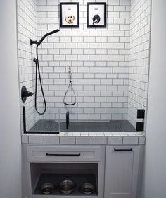 a white tiled bathroom with black and white tile on the wall, two pictures above the sink