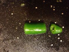 two green peppers sitting on top of a black counter next to white pepper flakes