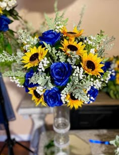 a bouquet of sunflowers and blue roses in a glass vase on a table