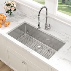 a stainless steel sink in a kitchen with marble counter tops and white cabinets next to a window