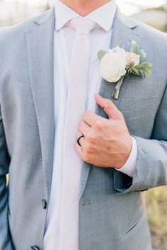 a man in a gray suit and white flower boutonniere is holding his hand on his lapel