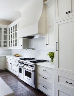 a kitchen with white cabinets and an oven in the middle of it, surrounded by wood flooring