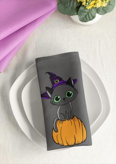 a napkin with a black cat wearing a witch's hat sitting on top of a white plate