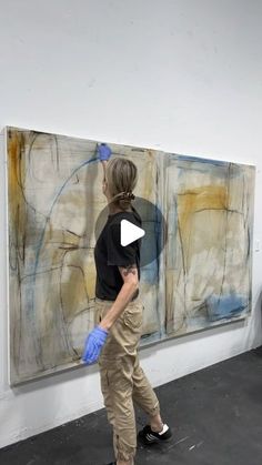 a woman standing in front of a painting with blue gloves on her hands and looking at it