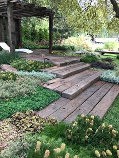 a wooden deck in the middle of a garden with flowers and plants growing on it