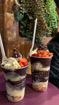 two ice cream sundaes with strawberries and chocolate on the top sitting on a table