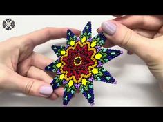 two hands are holding an ornament that looks like a star with colorful beads