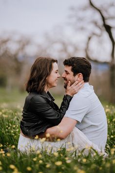 a man and woman are sitting in the grass with flowers around their necks looking at each other