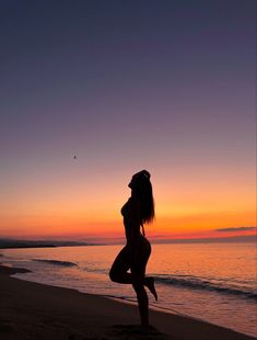 a woman standing on top of a sandy beach next to the ocean at sunset or dawn