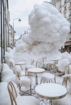 a group of tables and chairs covered in white fluffy clouds next to a building on a snowy street